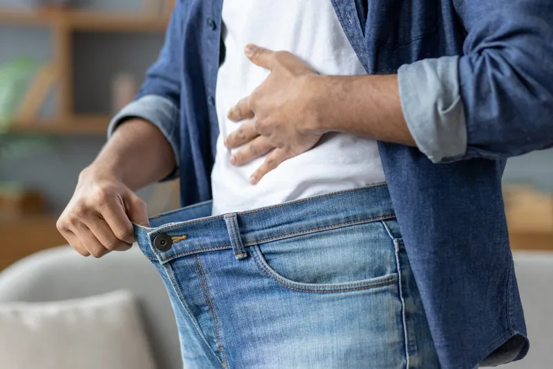 Man holding up loose jeans after weight loss