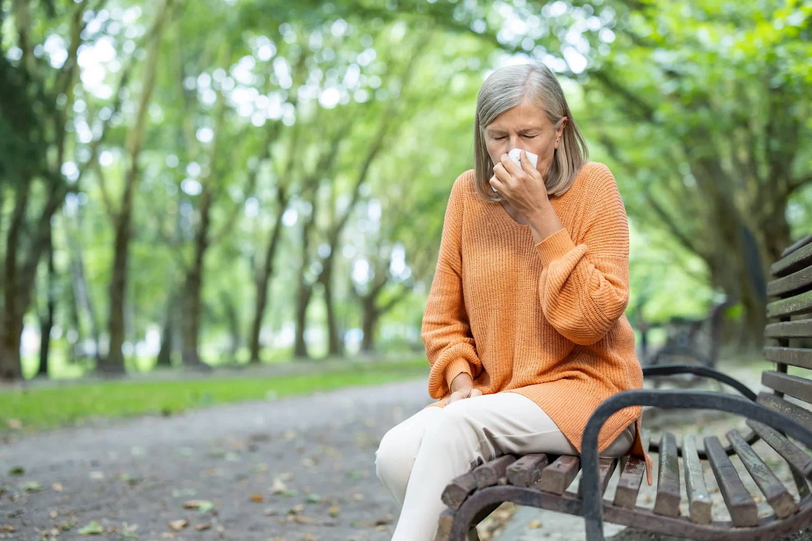 Woman with allergies sneezing in a park
